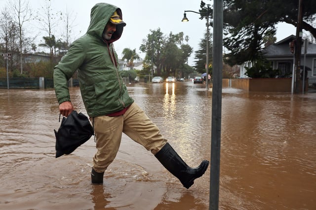 A person walks along a flooded street as a powerful long-duration atmospheric river, the second in less than a week, impacts California on Feb. 4, 2024, in Santa Barbara, Calif.