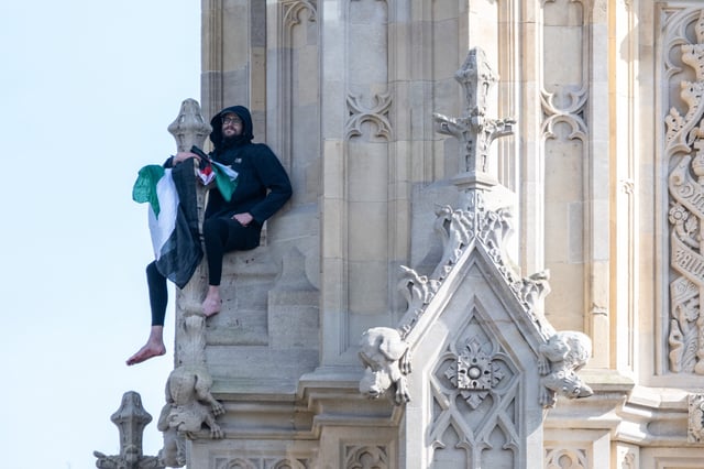 A man climbs up the side of the Elizabeth Tower with a flag in support of the Palestinian cause in London, UK.
