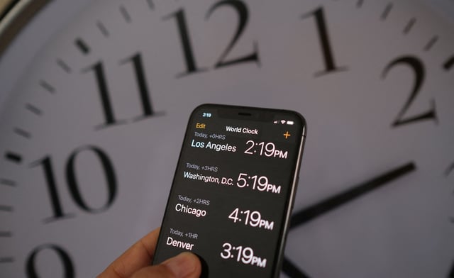 This illustration photo shows a clock in the background of a smartphone showing the time after daylight saving time was implemented in Los Angeles, California, on March 15, 2022.