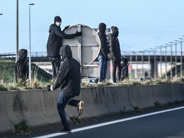 Migrants run across the A 16 motorway in an attempt to climb into the back of lorries bound for Britain while traffic is stopped upon waiting to board shuttles at the entrance to the Channel Tunnel site in Calais, northern France, on December 10, 2020. - The French port of Calais continues to attract migrants from the Middle East and Africa who set up makeshift camps while waiting to attempt to stow away on trucks heading across the Channel to England, with some attempting the crossing by boat. (Photo by DENIS CHARLET / AFP) (Photo by DENIS CHARLET/AFP via Getty Images)