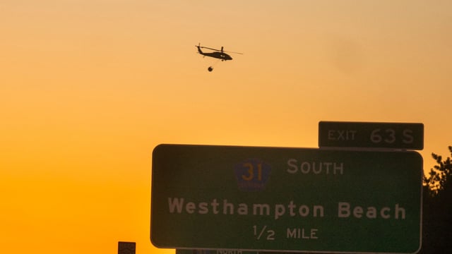 A rescue helicopter carries water along Route 27 on March 8, 2025 in Westhampton, New York. As strong winds fueled multiple brush fires on New York's Long Island, closing roads and reportedly burning structures (Photo by Andrew Theodorakis / GETTY IMAGES NORTH AMERICA / Getty Images via AFP)