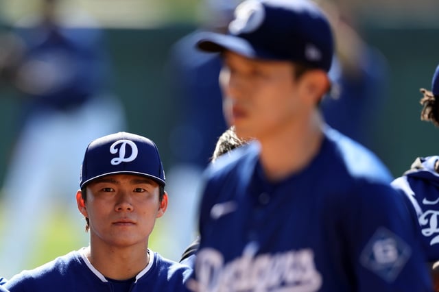 Yoshinobu Yamamoto looks on as Roki Sasaki throws a bullpen during workouts at Camelback Ranch.