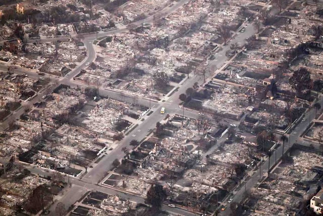 In an aerial view, an emergency vehicle (C) drives past destroyed homes as the Palisades Fire continues to burn on Jan. 09, 2025 in Pacific Palisades, California. Multiple wildfires fueled by intense Santa Ana Winds are burning across Los Angeles County. At least five people have been killed, and over 25,000 acres have burned. Over 2,000 structures have also burned and almost 180,000 people are under orders to evacuate. (Photo by Mario Tama/Getty Images)