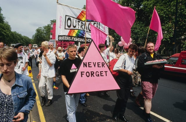 Marchers carrying a pink triangle with the words: 'Never Forget' at the Lesbian and Gay Pride event, London, 18th June 1994. The pink triangle began as a badge used at Nazi concentration camps to identify gay men. Behind the triangle is a banner for the gay rights campaign group, Outrage.