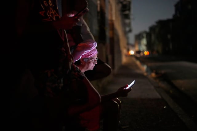 Residents look at their cell phones on the street during a general blackout in Havana, Cuba, Friday, March 14, 2025. (AP Photo/Ramon Espinosa)
