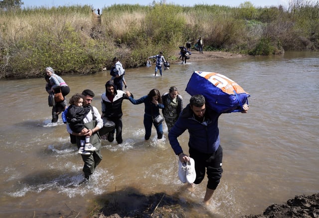 Syrian families who fled the clashes in Syria hold their luggages as they cross a river marking the border between Syria and northern Lebanon near the village of Heker al-Daher in Akkar province, Lebanon, Tuesday, March 11, 2025. (AP Photo/Hussein Malla)