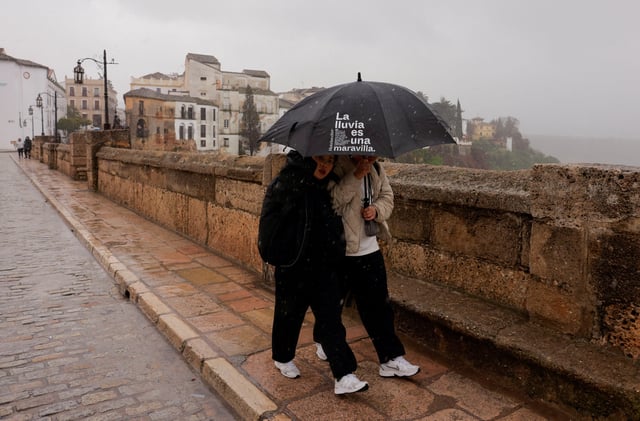 Tourists use an umbrella with a phrase that reads, "The rain is a wonder", to cover themselves from a heavy rain and high winds, while they tour the city centre along the New Bridge, as storm Konrad hits Spain, Portugal and France, in Ronda, Spain, March 13, 2025. REUTERS/Jon Nazca/File Photo