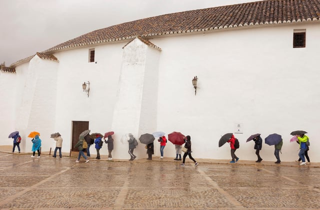 Tourists use umbrellas to cover themselves from a heavy rain and high winds, while they tour the city centre outside the bullring, as storm Konrad hits Spain, Portugal and France, in Ronda, Spain, March 13, 2025. REUTERS/Jon Nazca/File Photo
