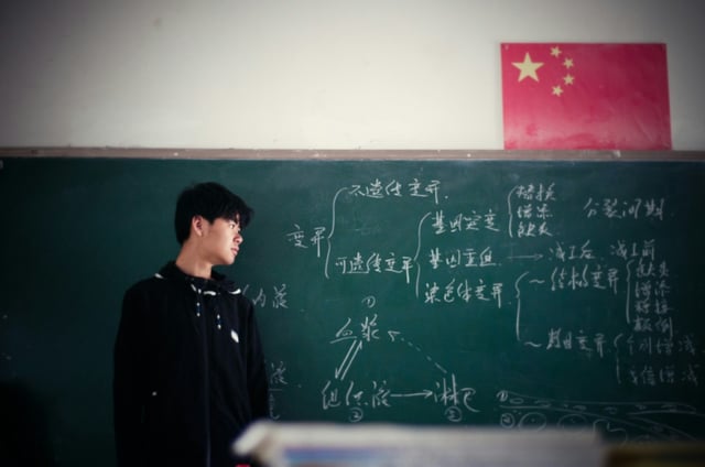 Chinese student standing in front of chalkboard and Chinese flag