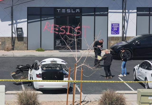 LAS VEGAS, NEVADA - MARCH 18: Investigators look over the scene at a Tesla Collision Center after an individual used incendiary devices to set several vehicles on fire on March 18, 2025 in Las Vegas, Nevada. The Las Vegas Metropolitan Police Department said that five Teslas were damaged and believe that the suspect fired three rounds from a firearm at the vehicles and spray painted the word "RESIST" on the entrance. (Photo by Ethan Miller/Getty Images)