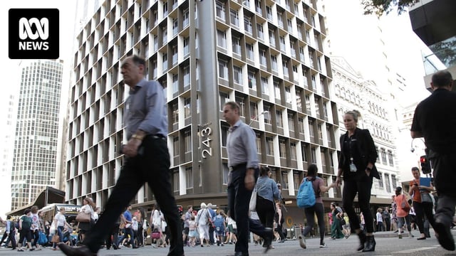 A number of people cross an intersection in Brisbane's CBD. Behind them are office buildings.
