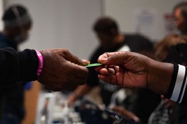 A poll worker hands a voter the green card used to identify the voter when using the machine to go to cast their vote on the first day of early voting at Metropolitan library on October 15, 2024 in Atlanta, Georgia.