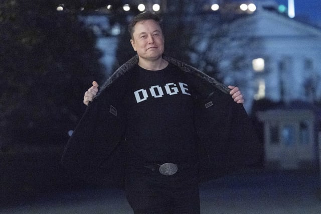 Elon Musk flashes his t-shirt that reads &#34;DOGE&#34; to the media as he walks on South Lawn of the White House, in Washington, Sunday, March 9, 2025.