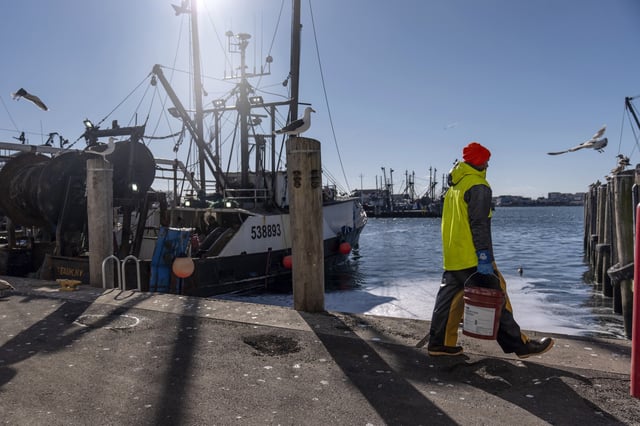 A fisherman carries supplies to a boat in the Port of Galilee, a fishing village in Narragansett, R.I., Wednesday, Jan. 15, 2025. (AP Photo/David Goldman)