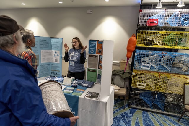 Lobstermen Roger Wilder, from left, and Glen Fernandes talk with Sarah Schumann, of the Fishery Friendly Climate Action Campaign, at her information table on ocean carbon capture at the Massachusetts Lobstermen's Association Annual Weekend and Trade Show, Friday, Jan. 31, 2025, in Hyannis, Mass. (AP Photo/David Goldman)