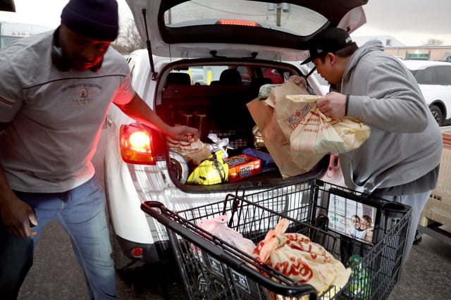 Albert Guerlley and Leo Rios load bags as cars line up to receive donated food at the Marie Wilkinson Food Pantry in Aurora, March 19, 2025. (Antonio Perez/Chicago Tribune)