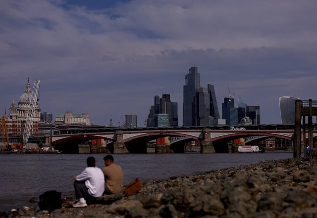 People sit on the bank of the river Thames in front of the financial district in London, Britain, August 27, 2024. REUTERS/Hannah McKay/File Photo