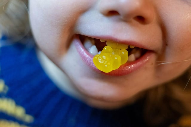 Ein Kind beißt auf ein Kinder-Vitaminbärchen