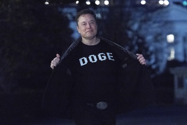 Elon Musk flashes his t-shirt that reads &#34;DOGE&#34; to the media as he walks on South Lawn of the White House, in Washington, Sunday, March 9, 2025.