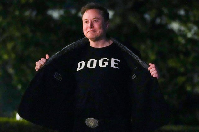Elon Musk shows off a shirt that says "DOGE" as he walks on the South Lawn of the White House on March 9, 2025.