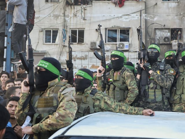 19.01.2025, Palästinensische Gebiete, Gaza-Stadt: Kämpfer der Qassam-Brigaden, des militärischen Flügels der Hamas, stehen auf einem Auto, als Fahrzeuge des Roten Kreuzes zur Abholung israelischer Geiseln, die im Rahmen eines Waffenstillstandsabkommens zwischen Israel und der Hamas freigelassen wurden, in Gaza-Stadt rangieren. Foto: Abed Hajjar/AP/dpa +++ dpa-Bildfunk +++