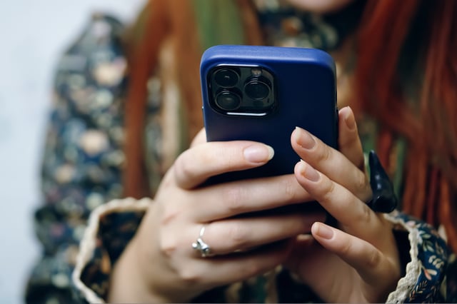 FILE - Woman blogger holds iPhone 13 pro in blue case and looks at screen. Smartphone in female&#39;s hands. Photos for advertising apps and gadgets. Bishkek, Kyrgyzstan - January 24, 2022.