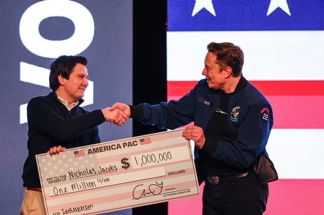 Elon Musk presents a check for $1 million dollars to a man during a town hall Sunday, March 30, 2025, in Green Bay, Wis. (AP Photo/Jeffrey Phelps)