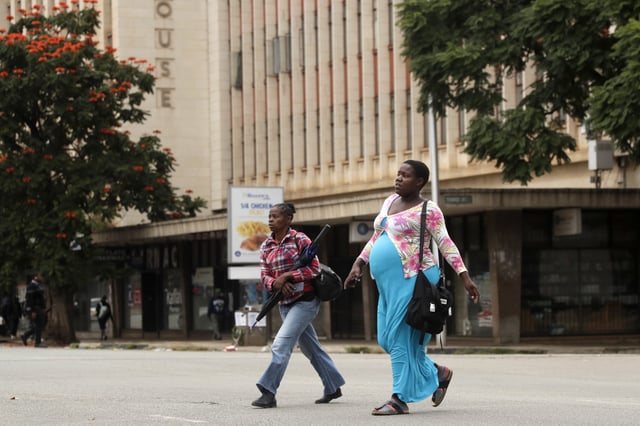 Women walk across a deserted street in downtown Harare, Zimbabwe, Monday, March 31, 2025, following calls for an anti-government protest. (AP Photo/Aaron Ufumeli)