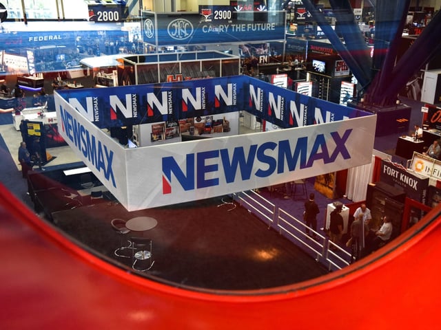 A Newsmax booth broadcasts as attendees try out the guns on display at the National Rifle Association (NRA) annual convention in Houston, Texas, on May 29, 2022.