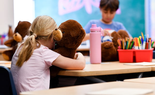 A student hugs a bear as she resumes class.