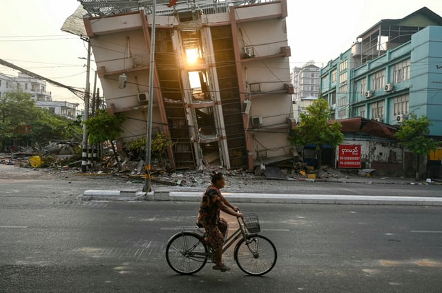 A woman rides her bicycle past a collapsed building in Mandalay on April 1, 2025, a few days after the deadly Myanmar earthquake. 