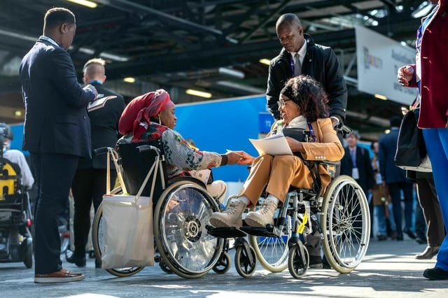 Zwei Besucherinnen im Rollstuhl sind auf dem Weltgipfel für Menschen mit Behinderungen und begrüßen sich