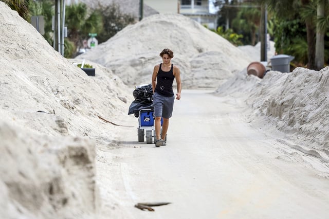 FILE - David DeMeza walks out with belongings through sands pushed on to the streets by Hurricane Helene, Oct. 2, 2024, in Treasure Island, Fla. (AP Photo/Mike Carlson, File)