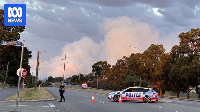 A police car blocks off a road in Ferndale in Perth's south as smoke from a bushfire billows into the sky in the background.