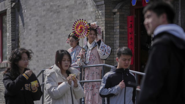 People walk by workers dressed in Qing Dynasty costumes, one of them holding a fan to attract customers outside a merchandise shop, in Beijing.