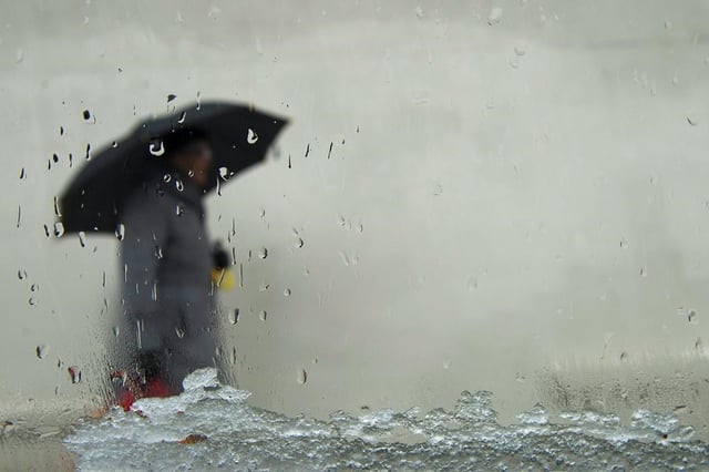 A woman, seen through a window, takes cover with her umbrella as both snow and rain fall in the streets of Toronto on Friday, Feb. 24, 2012. Environment Canada is warning of significant amounts of rain in Toronto and parts of the Greater Toronto Area that will make roads wet and slippery on Sunday. THE CANADIAN PRESS/Nathan Denette
