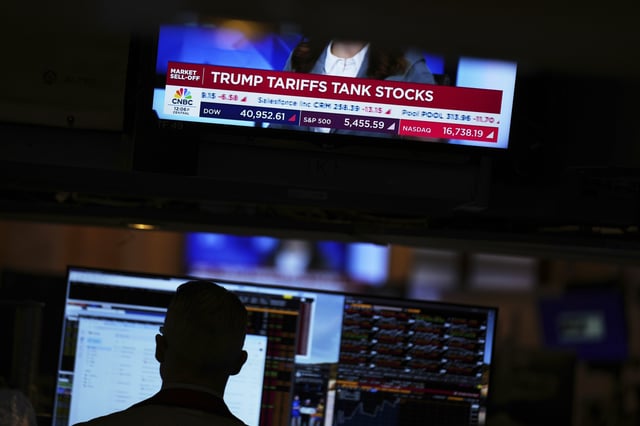 A screen displays financial news as traders work on the floor at the New York Stock Exchange in New York, Thursday, April 3, 2025. (AP Photo/Seth Wenig)