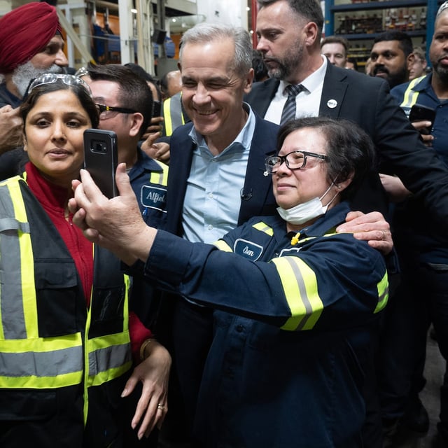 Workers pose with Liberal leader Mark Carney as he makes a campaign stop at an auto parts factory, Friday, April 4, 2025 in Vaughan.  THE CANADIAN PRESS/Adrian Wyld