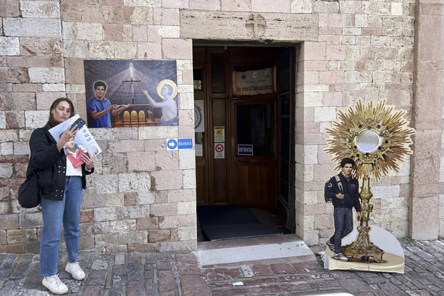 Amelia Simone, 18, a student from the United States, stands in front of the entrance of the Santa Maria Maggiore Church where the body of the 15-year-old Italian boy Carlo Acutis, who died in 2006 and was beatified in 2020, is kept, in Assisi, Italy, Wednesday, April 2, 2025. (AP Photo/Alessandra Tarantino)