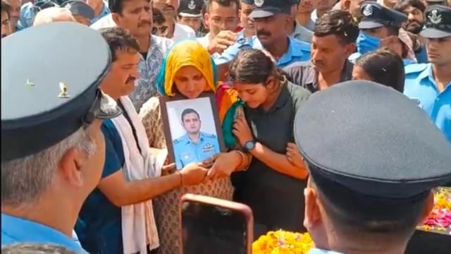 The parents and younger sister of flight lieutenant Siddharth Yadav holding his photo at his cremation in their native village of Majra Bhalkhi in Rewari district of Haryana on Friday. (HT Photo)