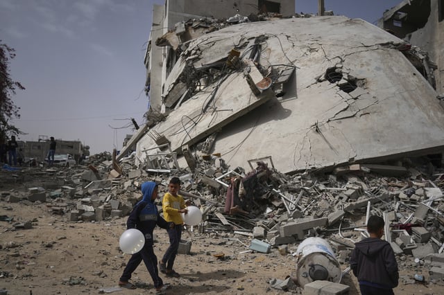 Children walk by the destroyed house of journalist Islam Meqdad, where she was killed along with her son and five other family members in an Israeli army strike in Khan Younis, southern Gaza Strip, Sunday, April 6, 2025. (AP Photo/Abdel Kareem Hana)