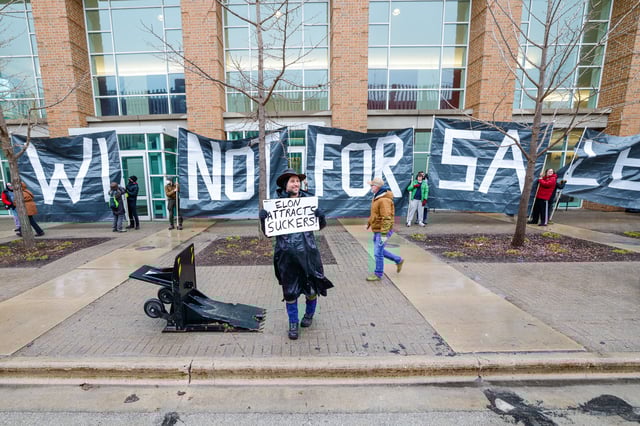 Protesters hold signs as people arrive for a town hall with Elon Musk, Sunday, March 30, 2025, in Green Bay, Wis. (AP Photo/Jeffrey Phelps)
