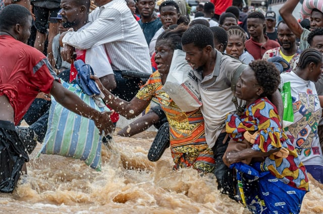 A man helps two women wade through the floodwaters in Kinshasa