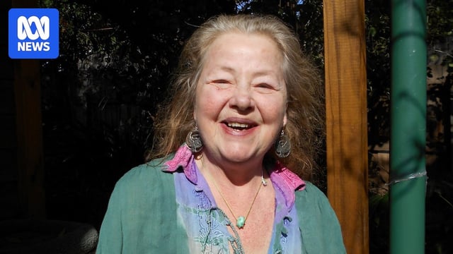 An old smiling woman, wearing a colourful shirt and green cardigan