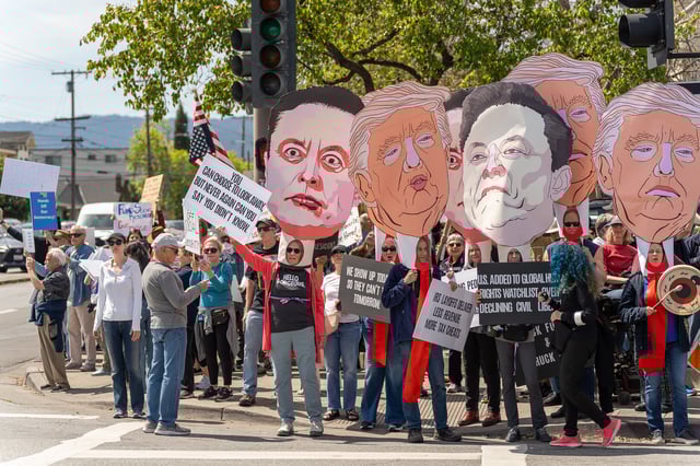 Protesters with local activist group Indivisible Portola Valley wave attneded the 'Hands Off' protest in Redwood City with gian cartoon cutouts of President Donald Trump and Elon Musk's faces on April 5, 2025. Photo by Anna Hoch-Kenney.