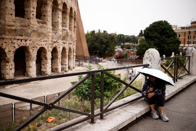 A woman holds an umbrella to shelter herself from the sun as she sits near the Colosseum amid a heatwave in Rome, Italy, June 20, 2024. REUTERS/Guglielmo Mangiapane/File Photo