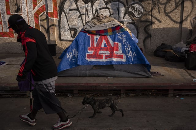FILE - A man walks past a homeless encampment in downtown Los Angeles, Wednesday, Oct. 25, 2023. (AP Photo/Jae C. Hong, File)