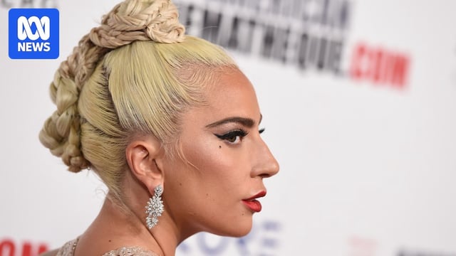 Close-up side profile of a blonde woman with large earrings and red lipstick on a red carpet.