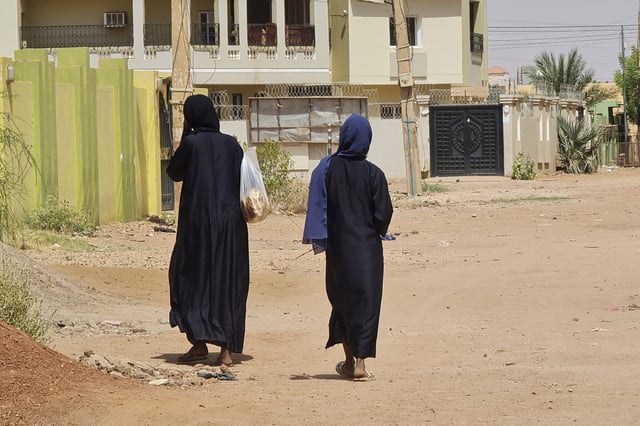 women carrying shopping bags walk on an empty street in Khartoum's Jabra neighbourhood, on May 28, 2023, as fighting between two rival generals persists. Since April 15, Sudan's capital and other cities have been gripped by brutal urban warfare between the regular army, the Sudanese Armed Forces (SAF), and the paramilitary Rapid Support Forces (RSF), leaving most banks shuttered, warehouses and factories looted, attacked and burned, with fuel in scarce supply, and civilians in need of urgent humanitarian aid. (Photo by AFP) (Photo by -/AFP via Getty Images)