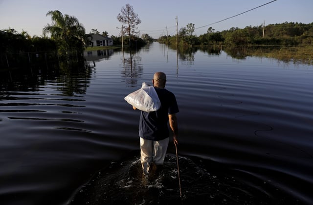 FILE - Jean Chatelier walks through a flooded street from Hurricane Irma after retrieving his uniform from his house to return to work today at a supermarket in Fort Myers, Fla., Sept. 12, 2017. (AP Photo/David Goldman, File)